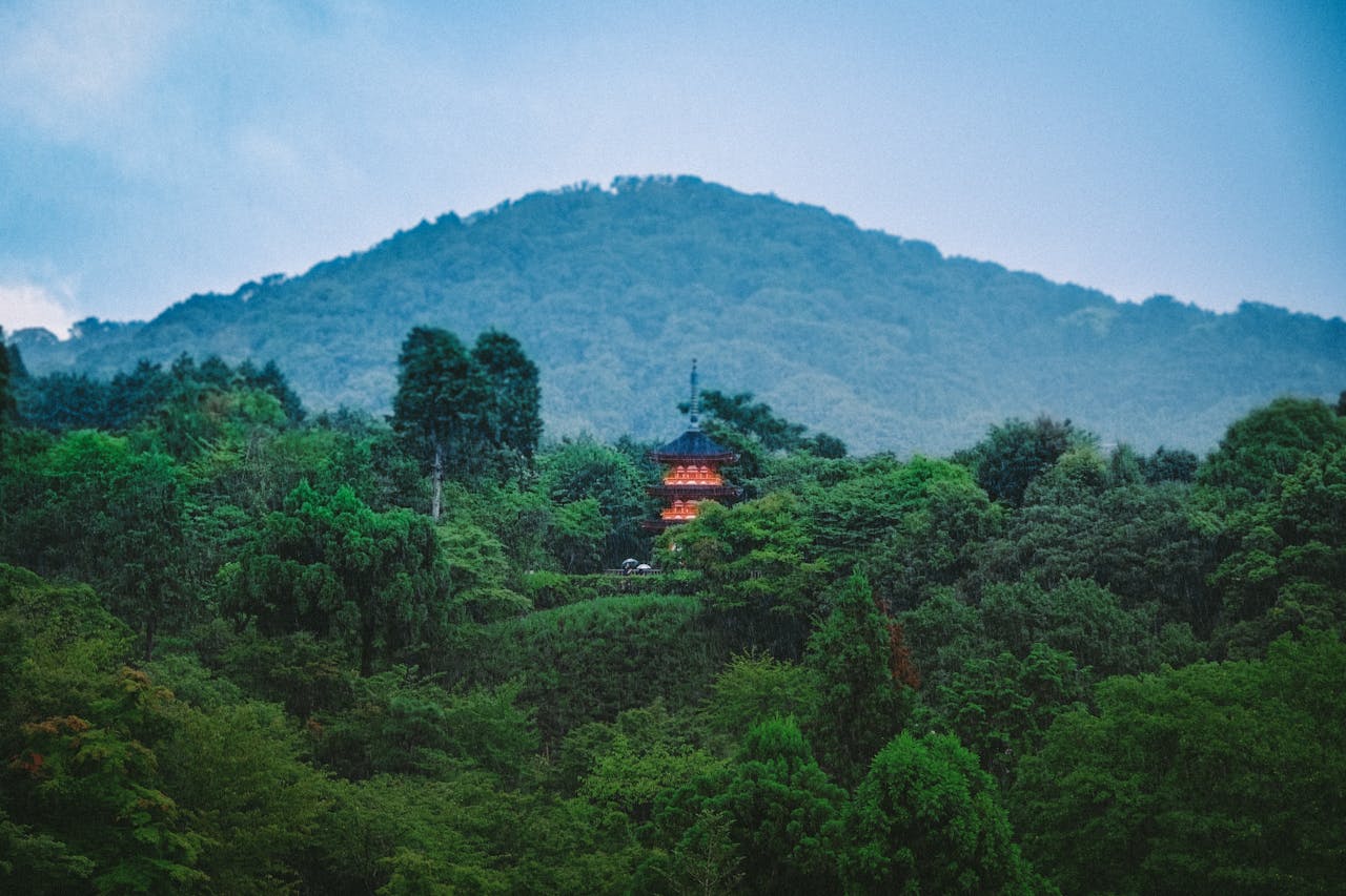 services-05 A tranquil scene featuring a pagoda nestled in lush greenery with a mountain backdrop at dusk.